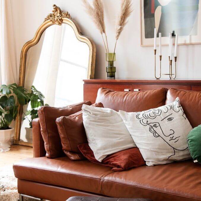 Parisian living room with brown leather sofa and gold leaning wall mirror