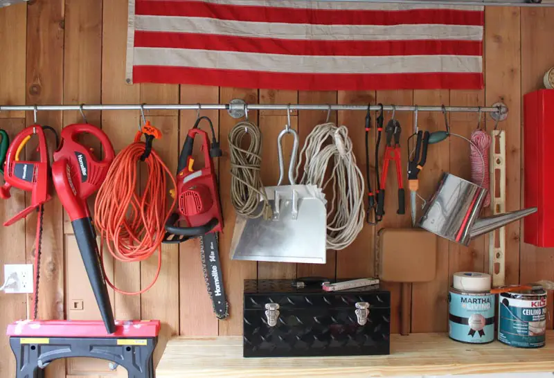 A metal rod mounted inside a shed, with s hooks for hanging power tools. 