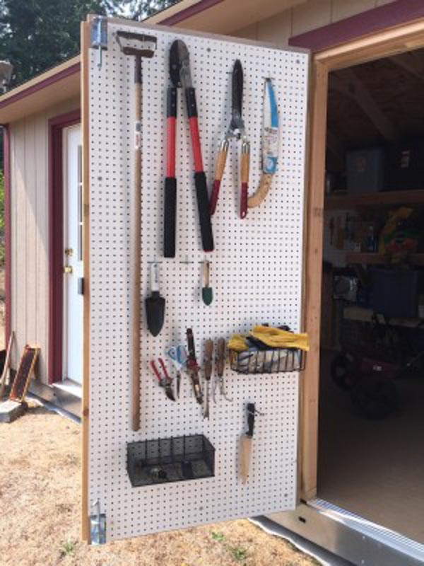 An opened workshop door covered with pegboard for holding hanging tools, for extra shed organization. 