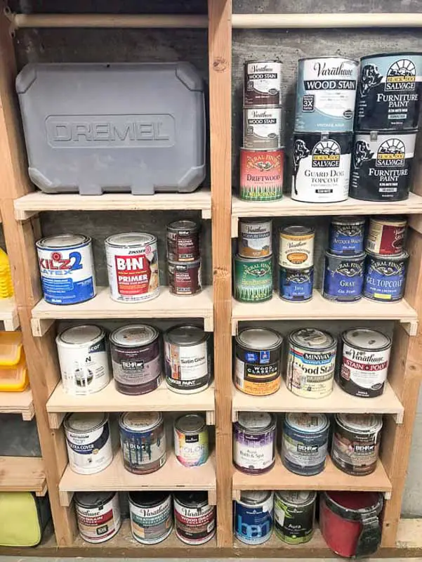 Small pieces of wood mounted between the studs of an outdoor shed for extra storage space. The shelves are filled with small cans of paint. 