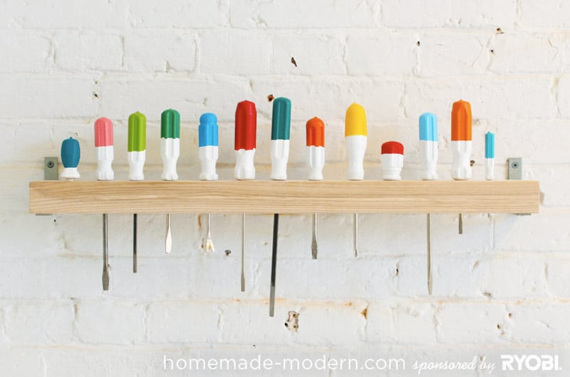 Screwdrivers with painted handles lined up in a wooden wall-mounted organizer. 