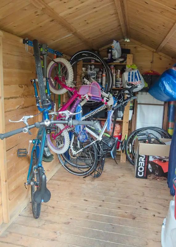 A shed with vertically mounted bicycles on the wall surrounded by other stored items. 