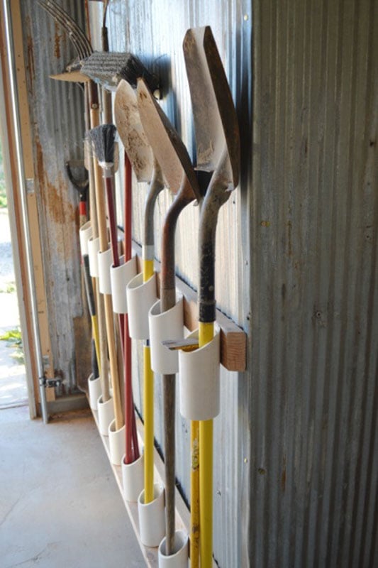 PVC pipe DIY tool organizer on a shed wall holding shovels, rakes and brooms. 