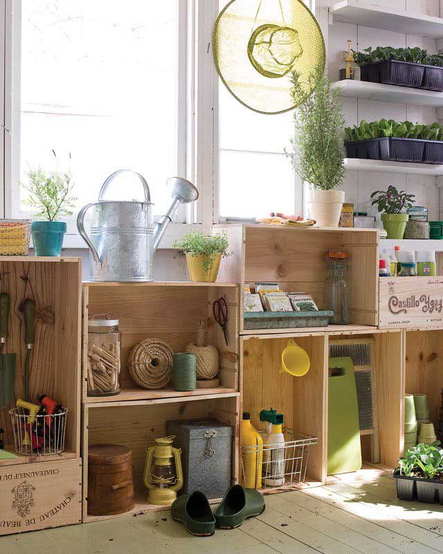 A collection of stacked wooden crates below a brightly lit window filled with gardening tools, supplies and potted plants. 