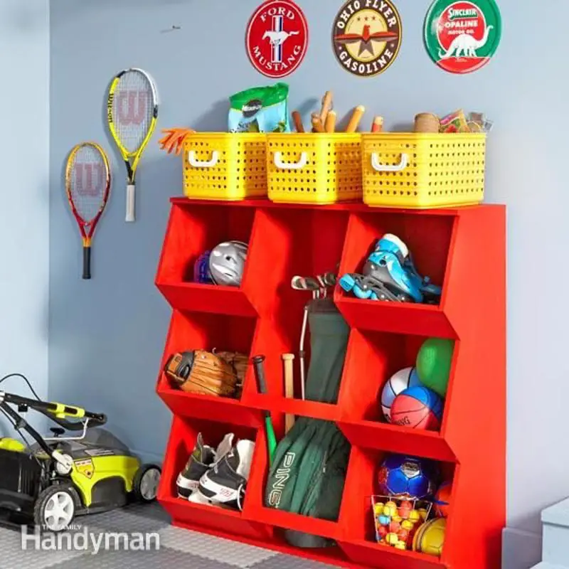 A red, wooden organizer DIY storing sports equipment, topped with three yellow baskets of gardening tools. 