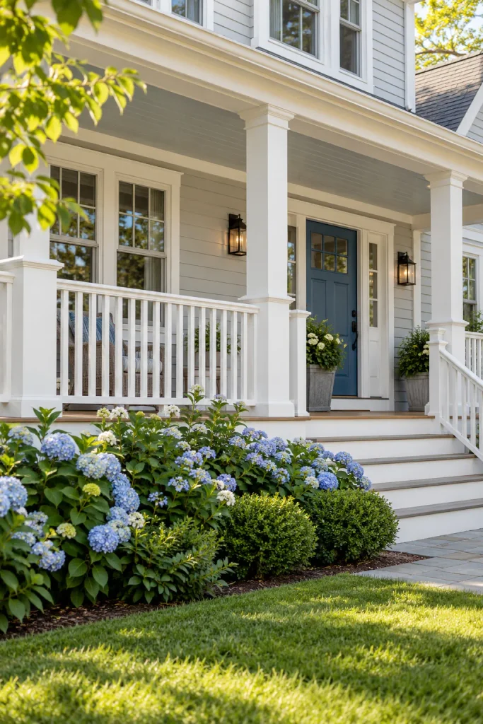 White square-baluster porch railing beside gray siding, a blue front door, and flowering hydrangeas.